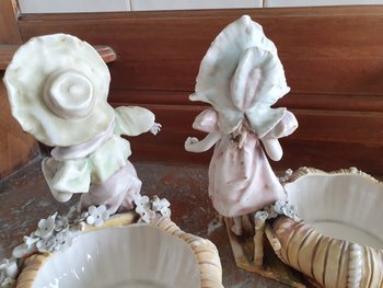 Bohemian-style porcelain figurines of children with shallow bowls, decorated with applique flowers dating to around 1900