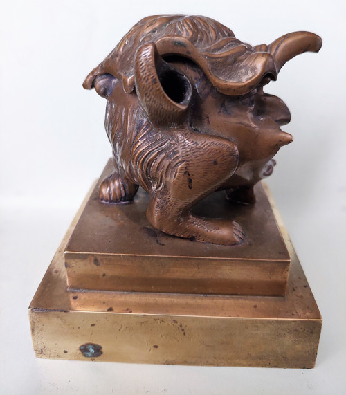 Old inkwell in gilded bronze on a base with the head of a laughing monster