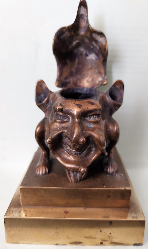 Old inkwell in gilded bronze on a base with the head of a laughing monster