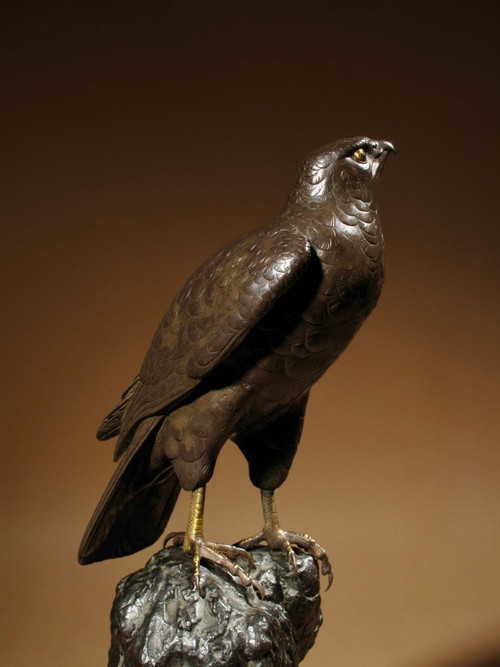 A highly decorative bronze model of a hawk sitting on a steep rock.