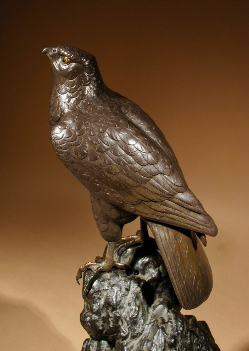 A highly decorative bronze model of a hawk sitting on a steep rock.