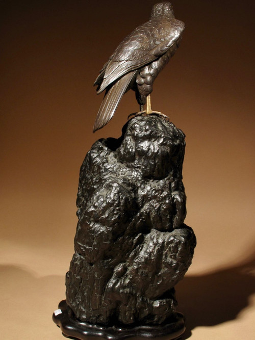 A highly decorative bronze model of a hawk sitting on a steep rock.