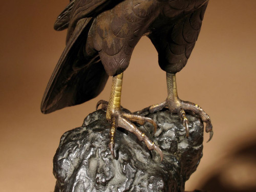 A highly decorative bronze model of a hawk sitting on a steep rock.