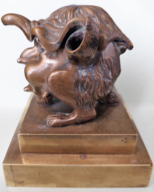 Old inkwell in gilded bronze on a base with the head of a laughing monster