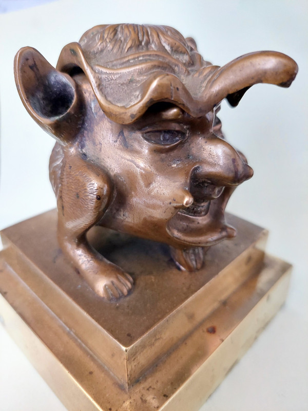 Old inkwell in gilded bronze on a base with the head of a laughing monster