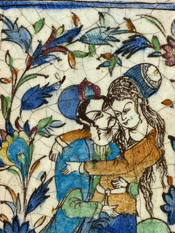 Enamelled tile representing an embracing couple in a stylized garden