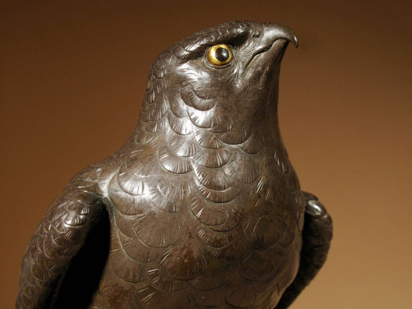 A highly decorative bronze model of a hawk sitting on a steep rock.