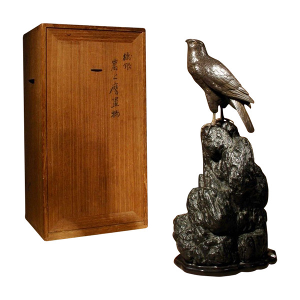 A highly decorative bronze model of a hawk sitting on a steep rock.